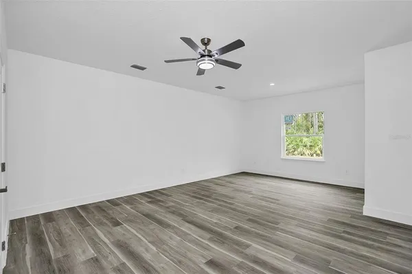 an empty room with wooden floor windows and fan