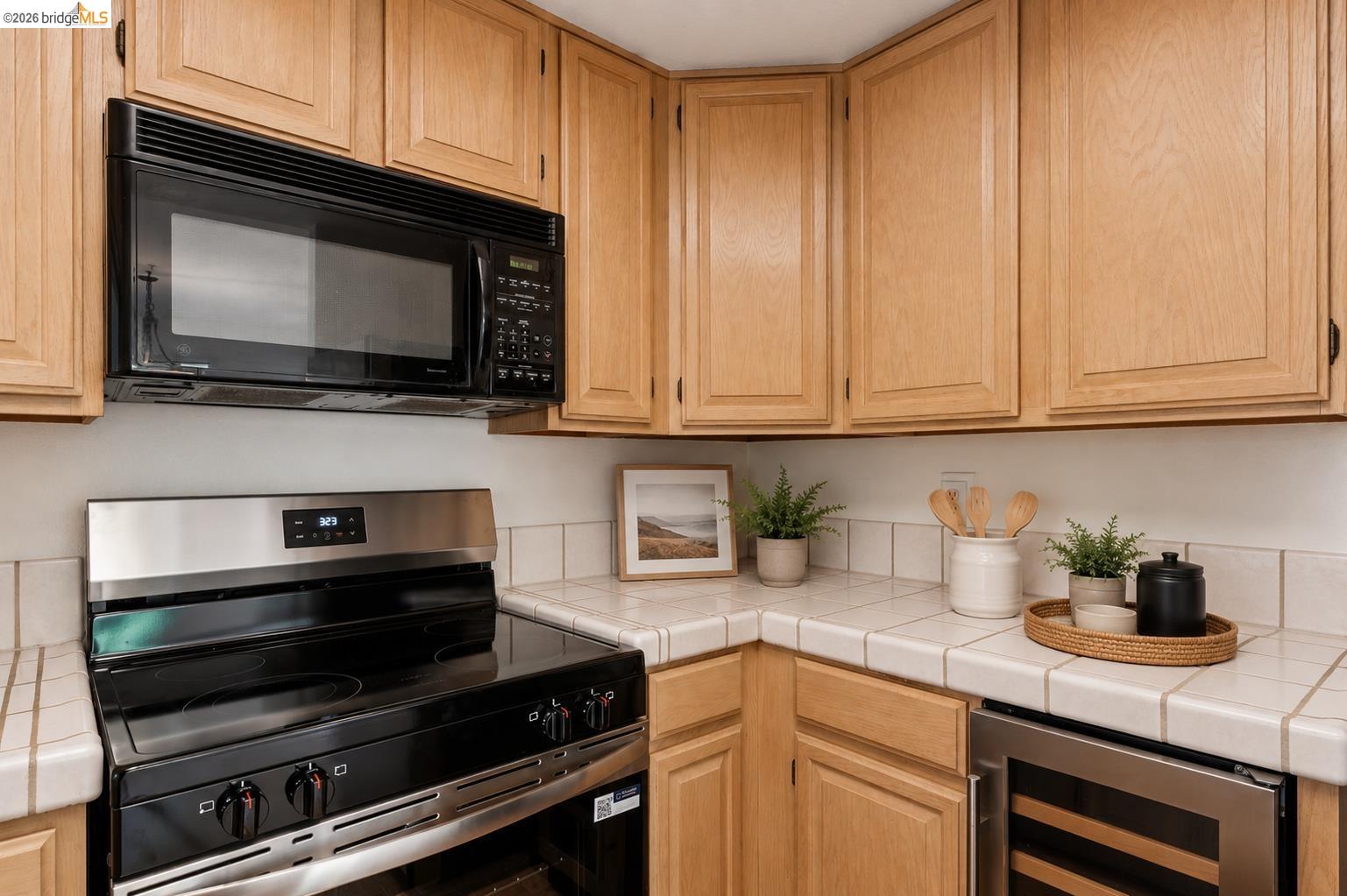 261 Redhawk Road Novato, CA 94949 - Photo 19 of 44 Wood-finish cabinetry and tiled countertops with an integrated stainless steel wine cooler, black electric range, and coordinating microwave