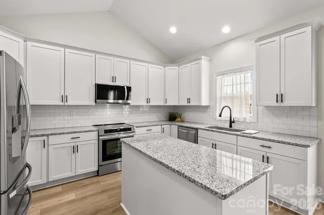 a kitchen with stainless steel appliances granite countertop a stove a sink dishwasher and a refrigerator with wooden floor