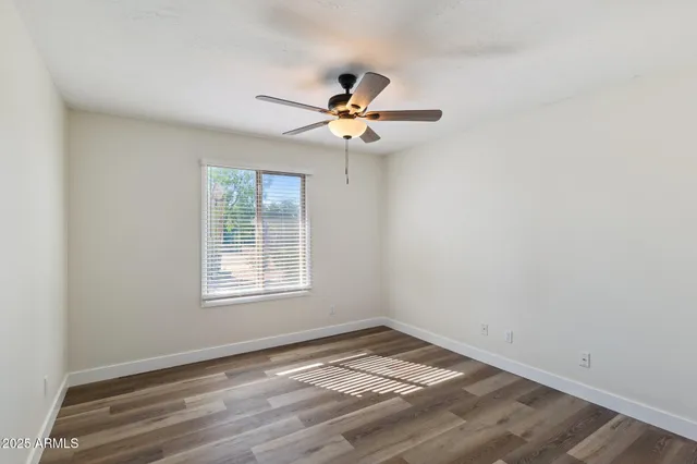an empty room with wooden floor ceiling fan and window