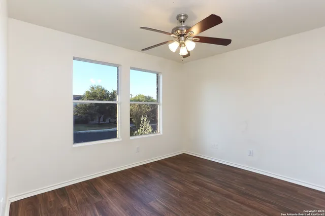 an empty room with wooden floor chandelier fan and windows