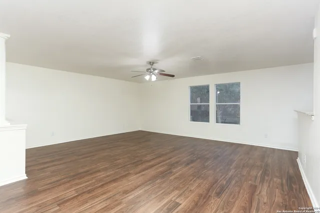 a view of empty room with wooden floor and fan