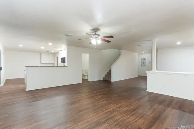 a view of an empty room with wooden floor and a kitchen
