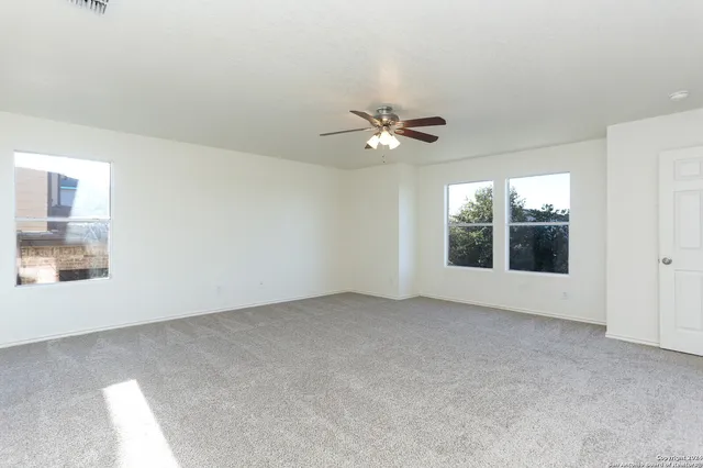 an empty room with chandelier fan and windows