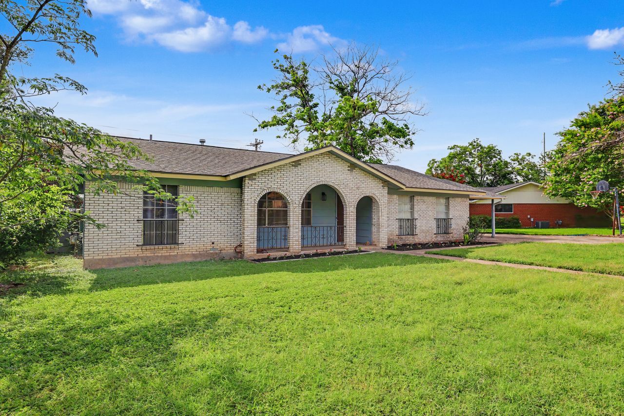 A well-maintained lawn welcomes you to this single-story home featuring a charming brick facade with arched entryways.