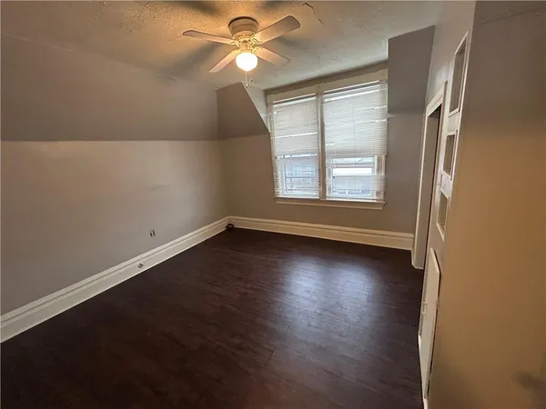 an empty room with wooden floor fan and windows