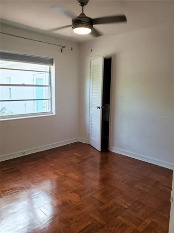 an empty room with wooden floor chandelier fan and windows