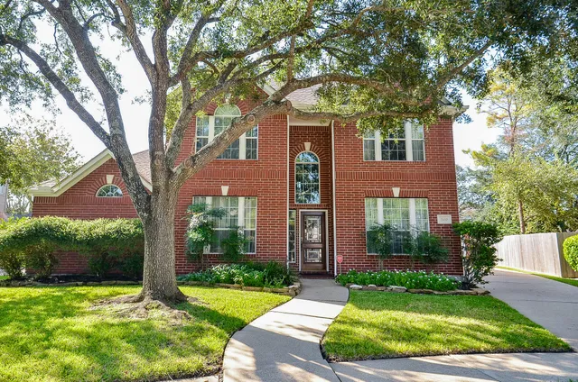 a view of a house with brick walls plants and large tree