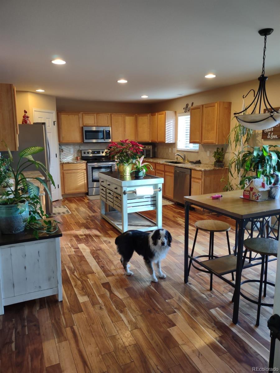 5342 Roadrunner Avenue Firestone, CO 80504 - Photo 11 of 21 a kitchen with stainless steel appliances kitchen island granite countertop a stove a sink a refrigerator and a dining table with wooden floor