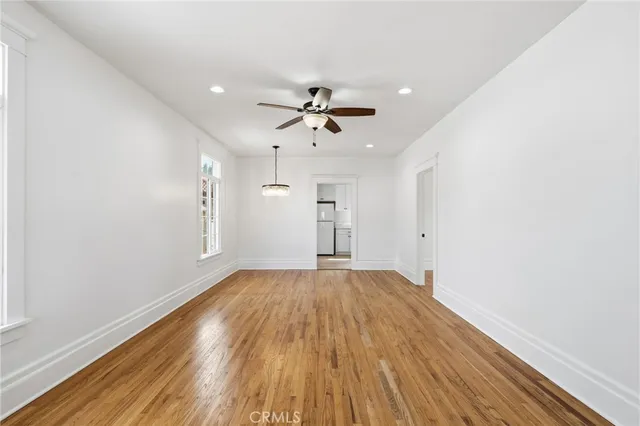 an empty room with wooden floor ceiling fan and windows