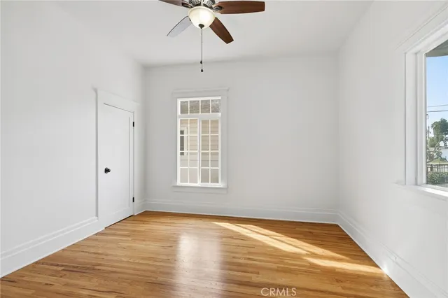 an empty room with wooden floor fan and windows