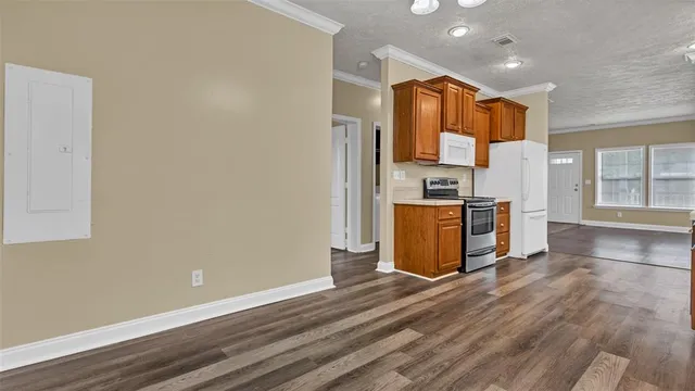 an empty room with wooden floor and kitchen view