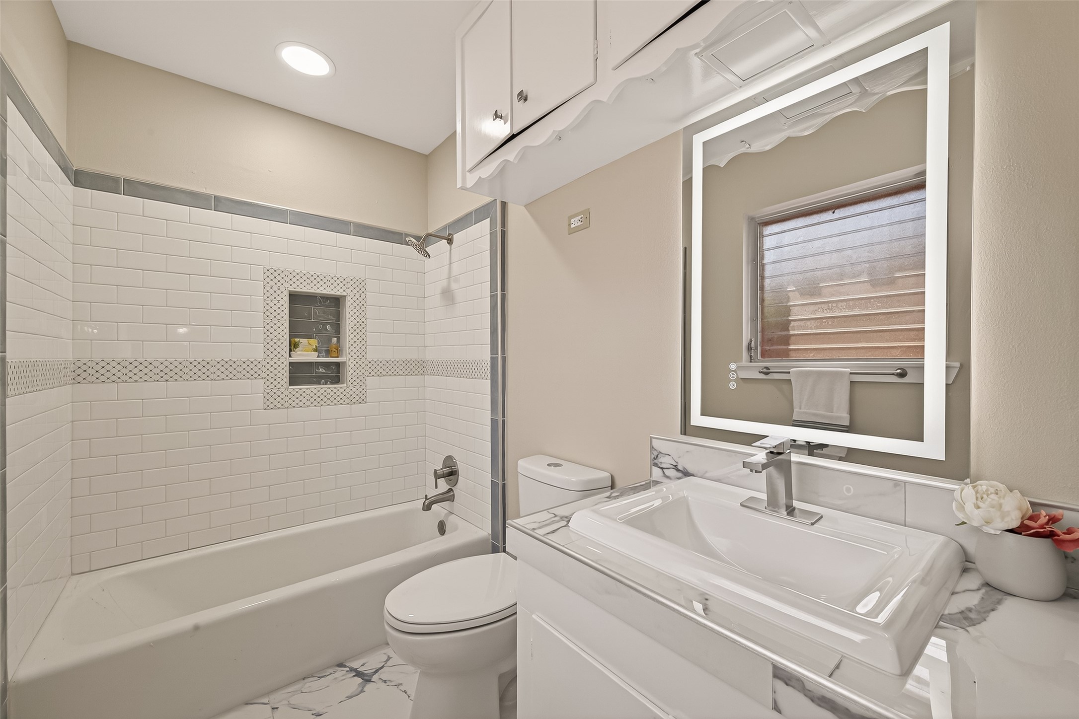 5646 Hazen Street Houston, TX 77081 - Photo 24 of 43 This primary bathroom highlights a modern design with an illuminating mirror, sleek fixtures, and a stylish tiled shower-tub combo.