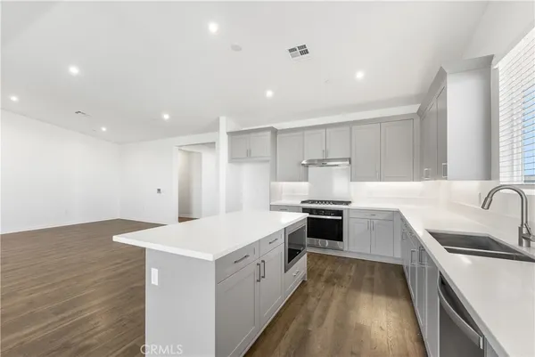 a large white kitchen with a stove top oven a sink a refrigerator and white cabinets with wooden floor