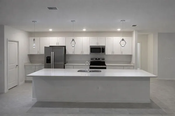 a large kitchen with stainless steel appliances a refrigerator a stove a microwave and white cabinets