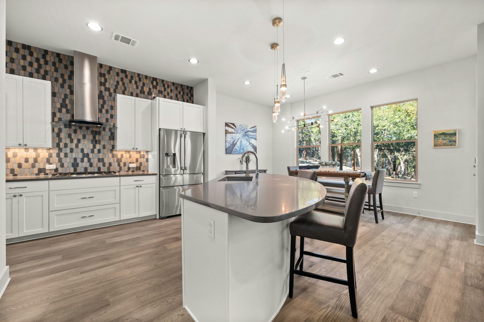 8110 Ranch Road 2222, Unit 92 Austin, TX 78730 - Photo 7 of 40 Modern kitchen featuring white cabinetry, stainless steel appliances, a geometric tile backsplash, a curved island with seating, and wood-finish flooring