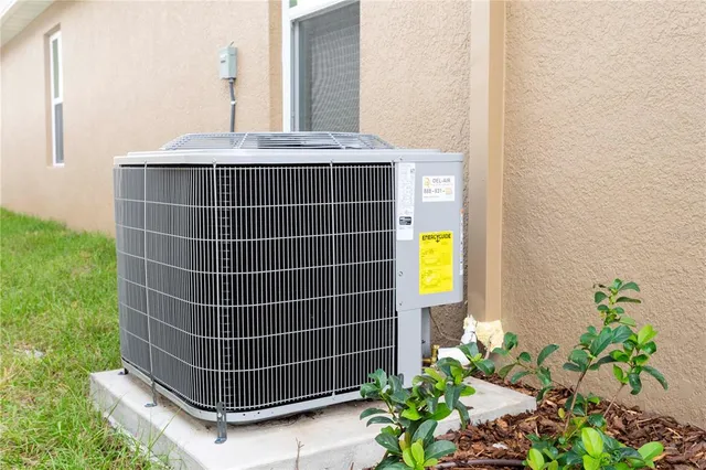 a view of a brick house with a yard plants and large tree