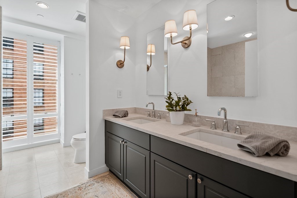 80 Broad Street, Unit 902 Boston, MA 02110 - Photo 11 of 30 a bathroom with a granite countertop sink a toilet and a large mirror