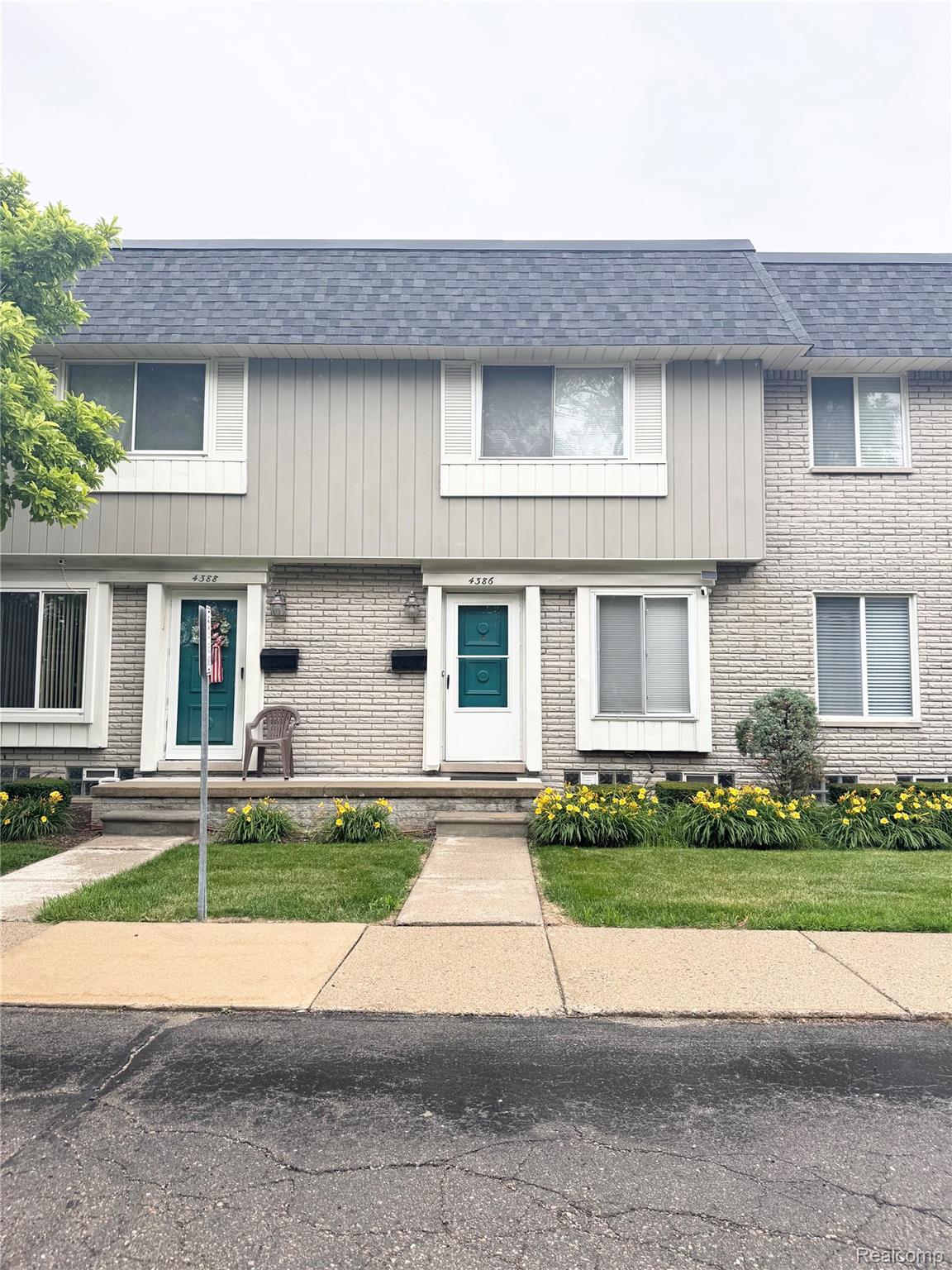 4386 15 Mile Road, Unit 64 Sterling Heights, MI 48310 - Photo 1 of 23 Townhome exterior featuring a brick and vertical siding facade, a dark shingle roof, white trim windows, and teal entry doors
