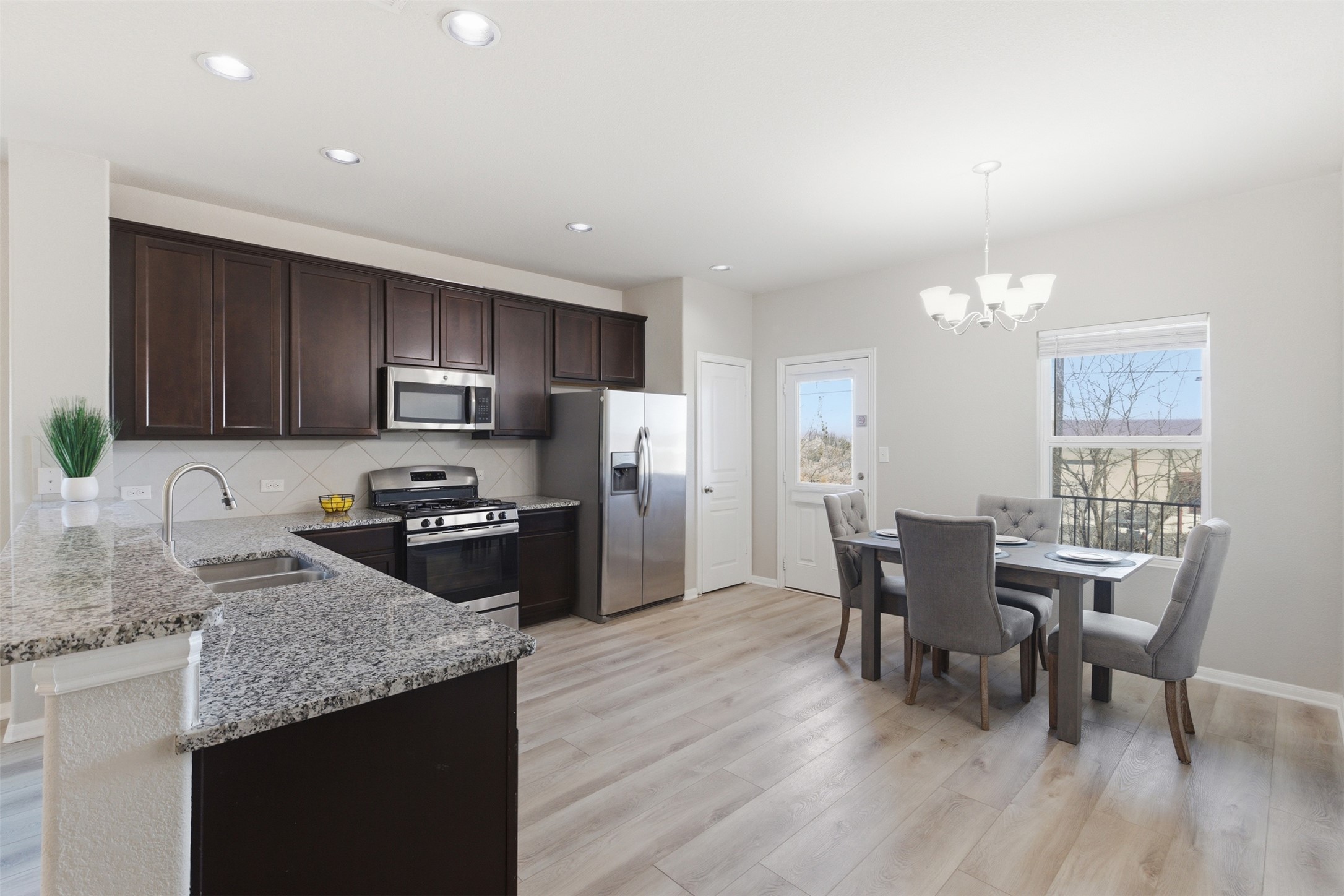 480 Waterloo Drive Kyle, TX 78640 - Photo 5 of 23 Kitchen featuring dark wood finish cabinets, stainless steel appliances, light stone counters, tasteful backsplash, and light wood-style floors