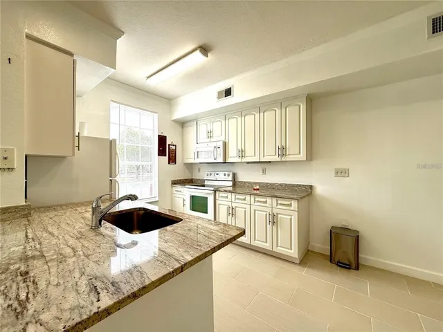 a kitchen with granite countertop a sink a stove top oven a counter space and cabinets