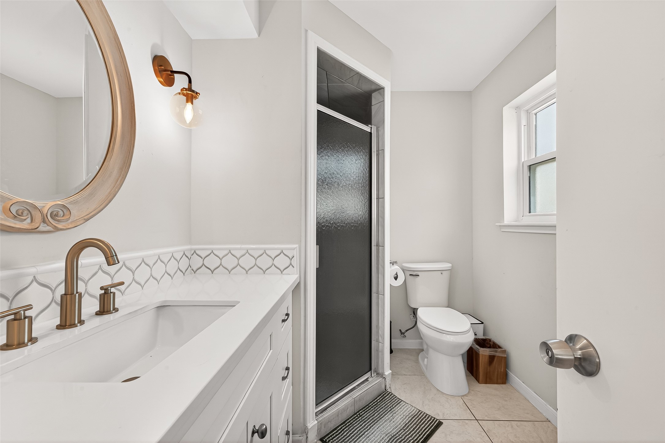 2610 Teague Road Houston, TX 77080 - Photo 33 of 49 This primary bathroom features a modern design with a large mirrored vanity, elegant fixtures, and a sleek glass shower. Natural light illuminates the space through a window, creating a bright and welcoming atmosphere.