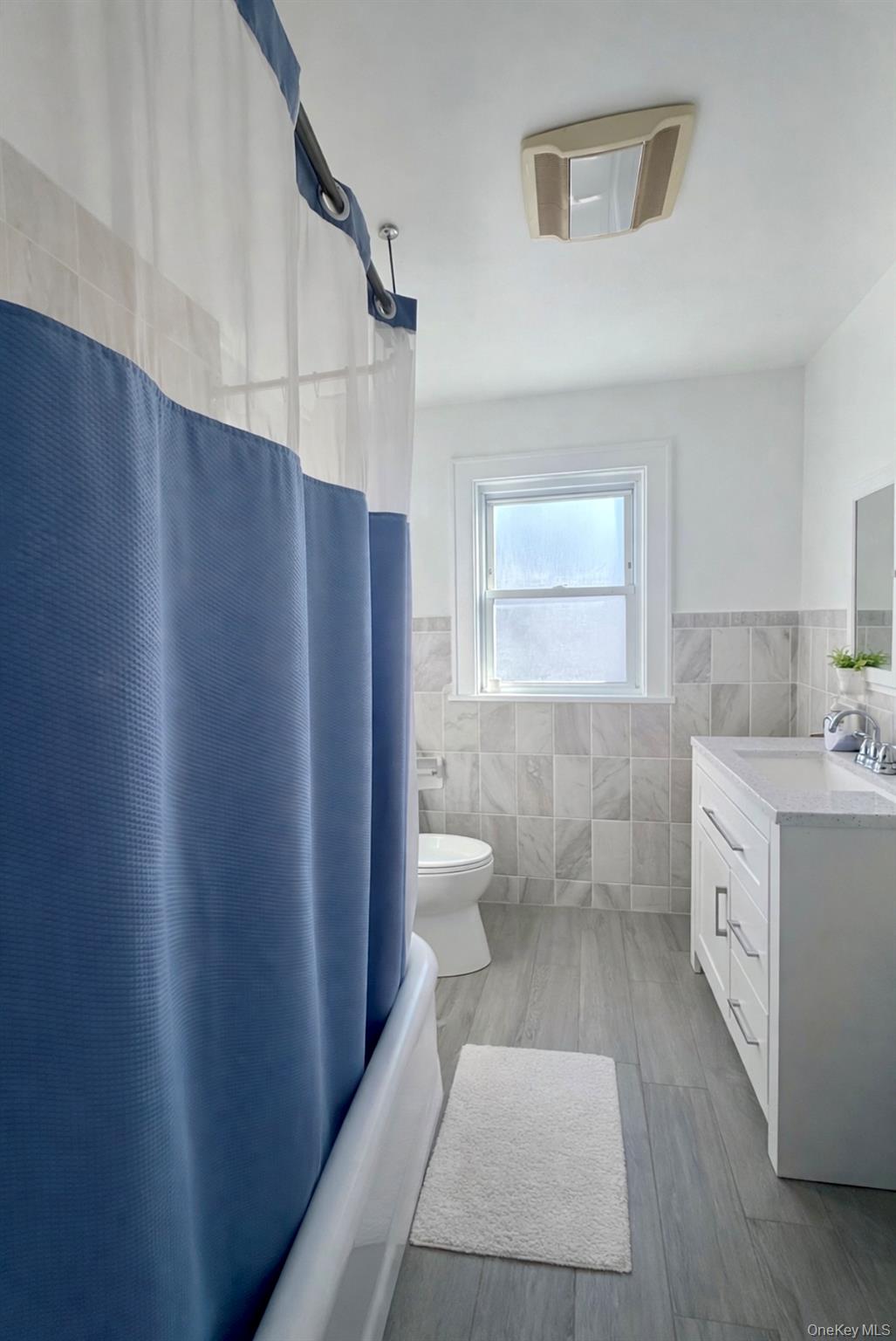 130 Clinton Avenue, Unit 2 New Rochelle, NY 10801 - Photo 6 of 6 Full bathroom with tile walls, wainscoting, shower / bath combo with shower curtain, vanity, and light wood-type flooring
