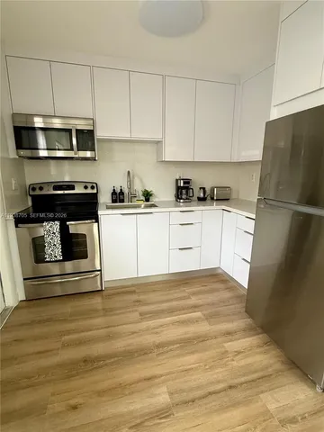 a kitchen with granite countertop a refrigerator stove and white cabinets