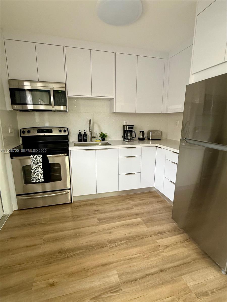 864 80th Street, Unit 1 Miami Beach, FL 33141 - Photo 7 of 13 a kitchen with granite countertop a refrigerator stove and white cabinets