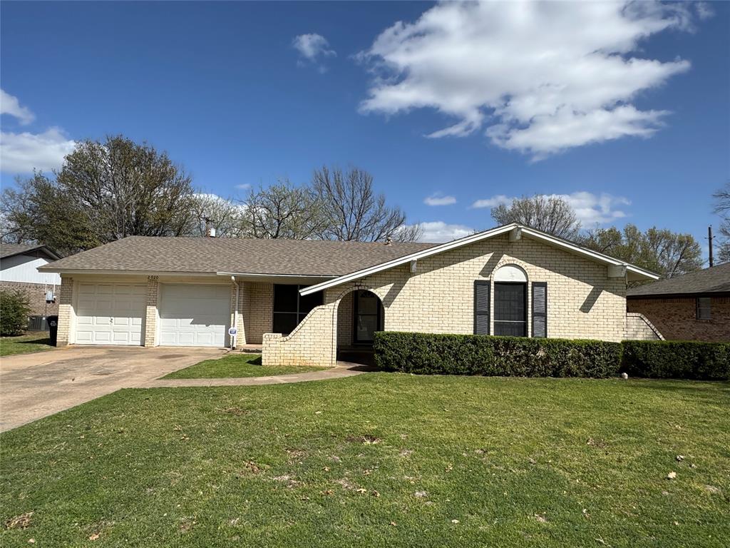 Ranch-style home with driveway, a front yard, brick siding, a garage, and a shingled roof