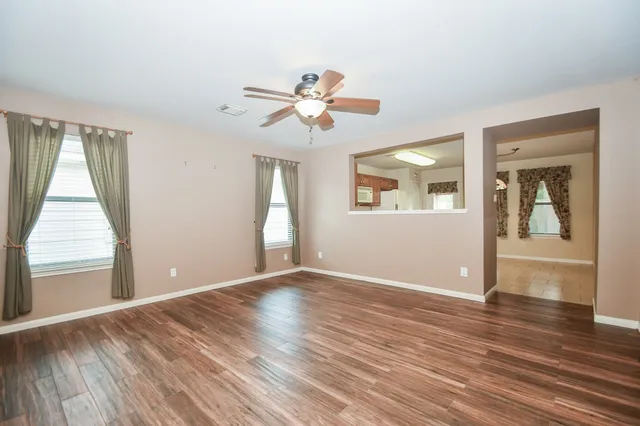 an empty room with wooden floor chandelier fan and windows