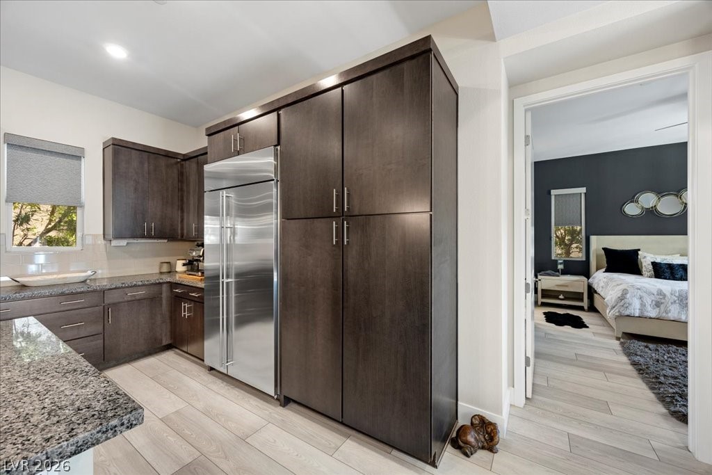 4262 Swift Street Las Vegas, NV 89135 - Photo 21 of 75 Kitchen featuring dark brown cabinets, stainless steel built in refrigerator, light stone counters, and light wood finished floors