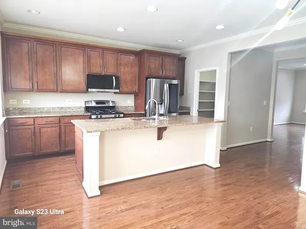 a kitchen with stainless steel appliances granite countertop a stove top oven a sink a refrigerator and white cabinets with wooden floor