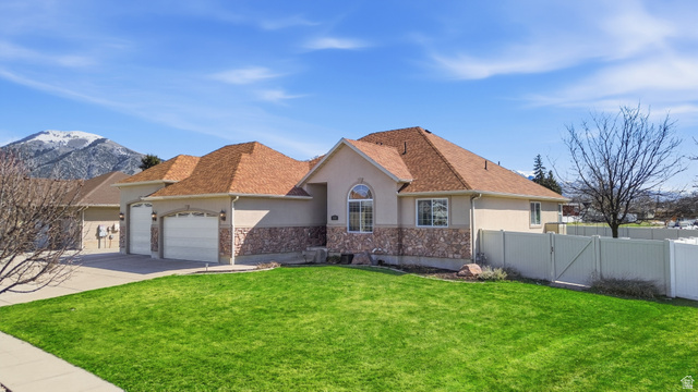 860 West 2980th Street South Logan, UT 84321 - Photo 2 of 38 Exterior featuring stucco siding with stone accents, a multi-car garage, a well-maintained lawn, and a light-colored privacy fence