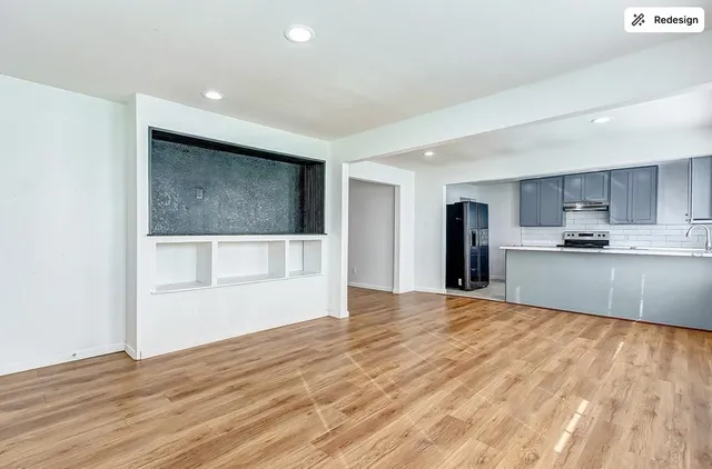 a view of empty room with wooden floor and kitchen