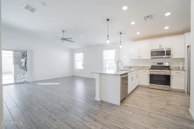 a kitchen with stainless steel appliances kitchen island granite countertop a stove a sink a refrigerator and white cabinets with wooden floor