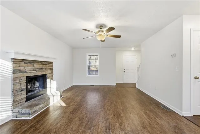 an empty room with wooden floor a fireplace a ceiling fan and windows