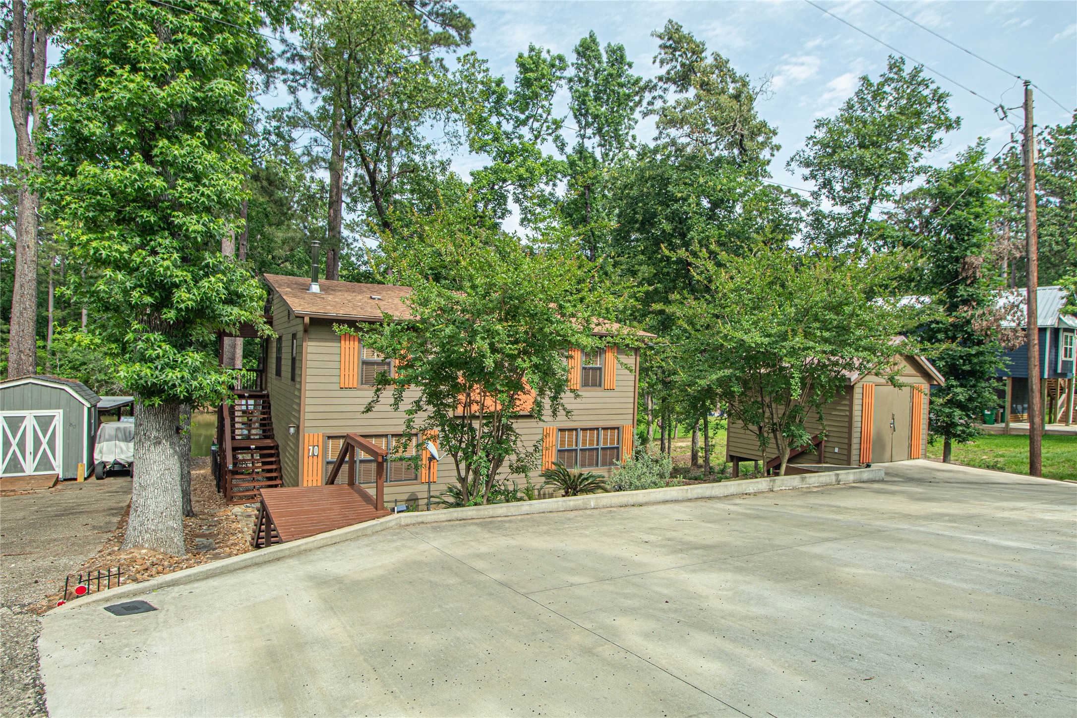 70 Lower Cove Drive Point Blank, TX 77364 - Photo 9 of 50 Home is taupe and burnt orange nestled into the hill side and surrounded by trees! The large concrete pad was installed by this seller to provide ample parking. To the right, also added, a storage building for a golf cart and other items.