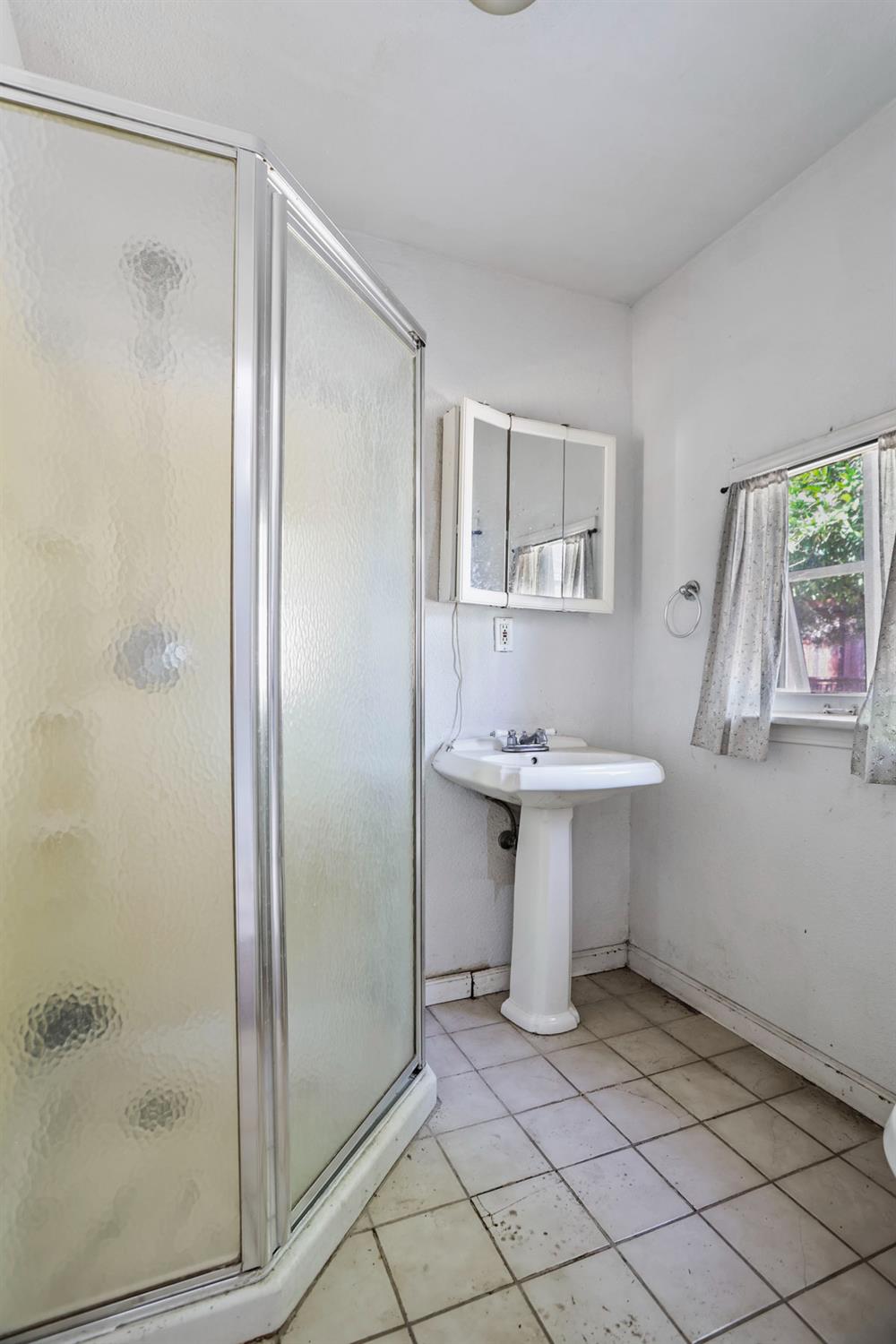 916 Elm Avenue Modesto, CA 95351 - Photo 48 of 52 Compact rear unit bathroom with shower enclosure, pedestal sink, toilet, tile flooring, and natural light.