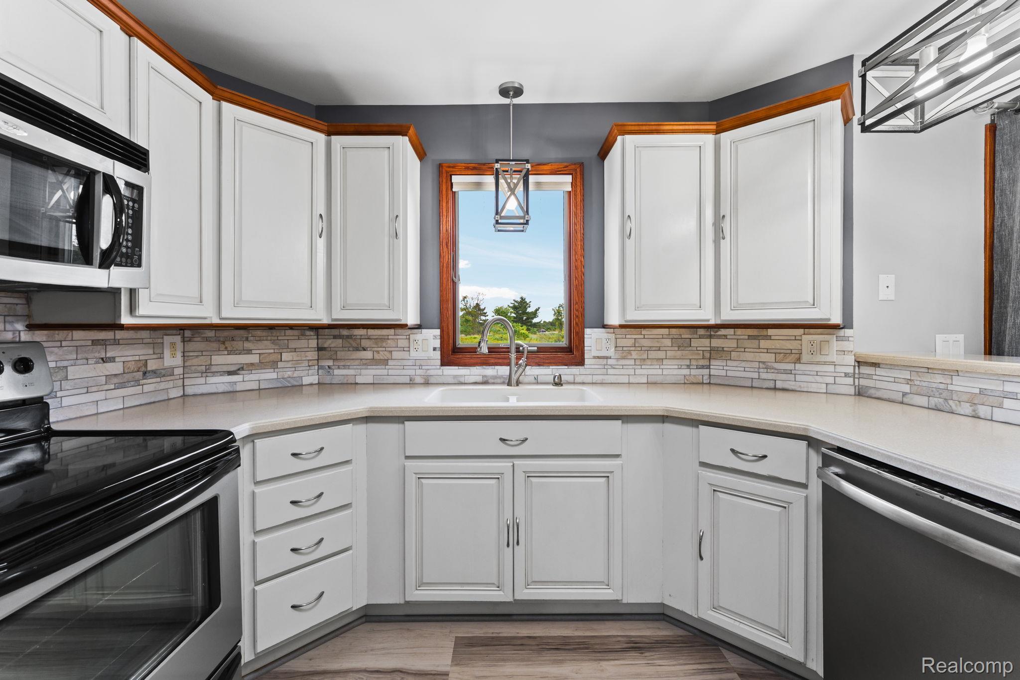 2381 Burke Road Fowlerville, MI 48836 - Photo 8 of 31 Kitchen featuring white cabinetry with wood trim, a stone tile backsplash, light-toned countertops, and corian sink with a gooseneck faucet.