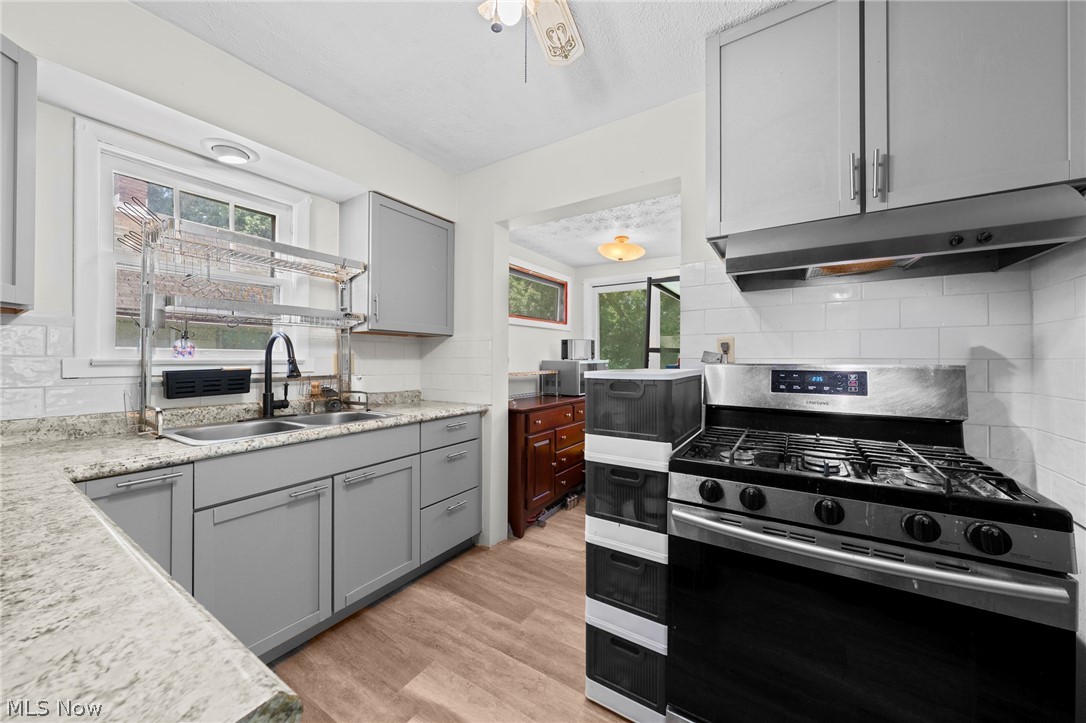 819 Keeney Street Akron, OH 44310 - Photo 23 of 24 Kitchen featuring light gray cabinetry, light-toned granite-style countertops, subway tile backsplash, wood-finish flooring, and a stainless steel gas range with overhead ventilation