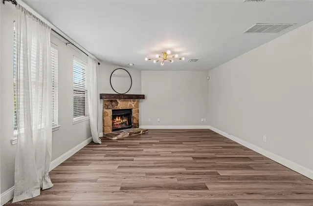 a view of an empty room with wooden floor fireplace and a window
