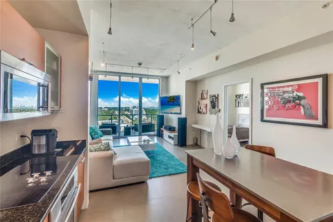 a living room with stainless steel appliances furniture a large window and a kitchen view