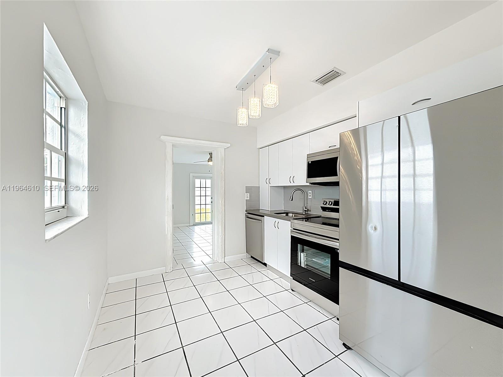 6819 Southwest 25th Street Miami, FL 33155 - Photo 5 of 25 a large kitchen with white cabinets stainless steel appliances and a window