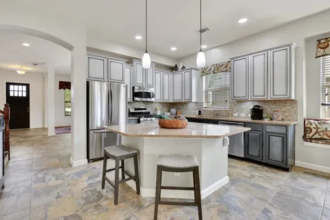 a kitchen with kitchen island granite countertop a stove a refrigerator a oven a sink with island chairs and wooden cabinets