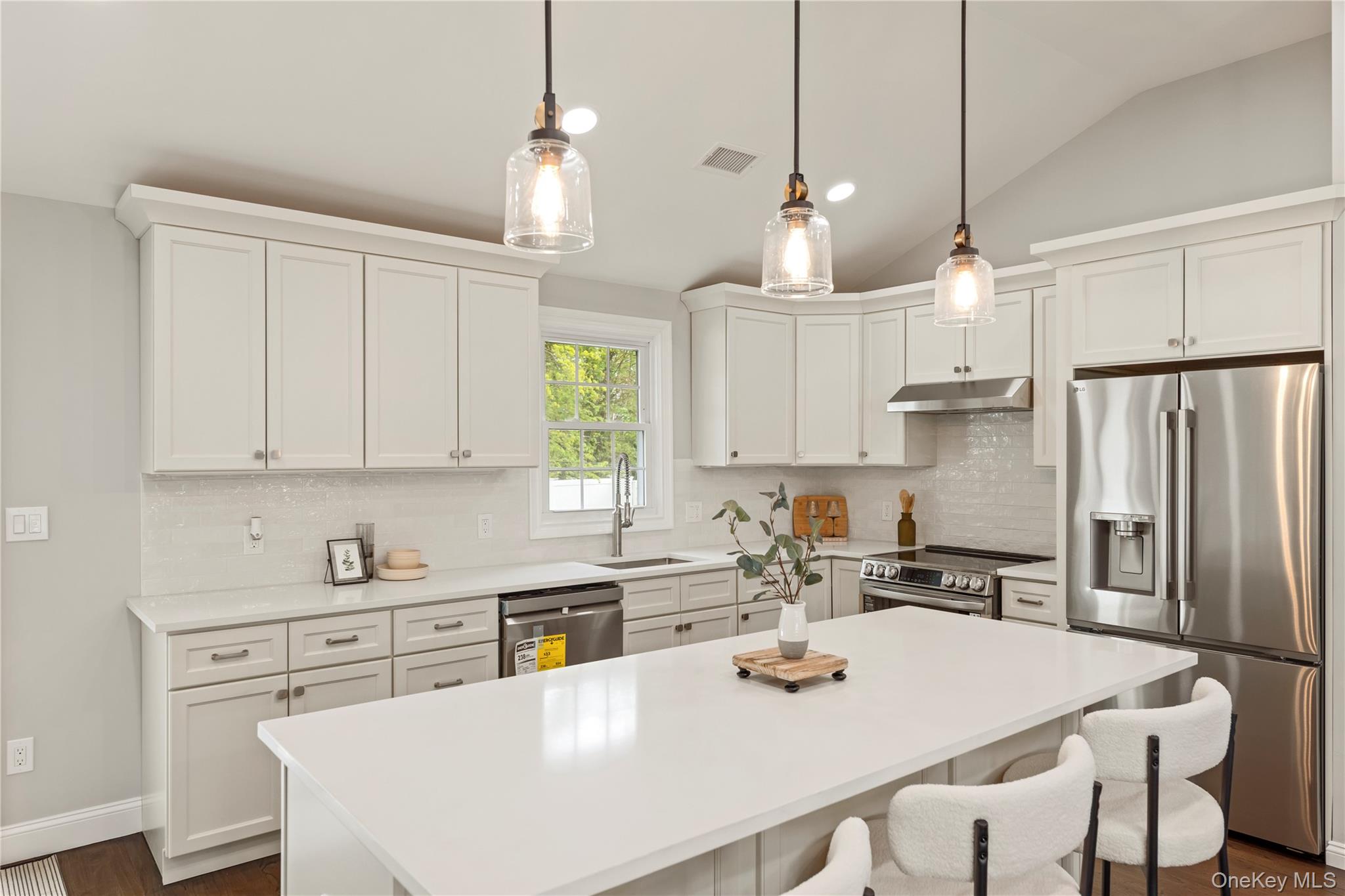 16 Eleanor Road Plainview, NY 11803 - Photo 8 of 28 Modern kitchen featuring white cabinetry, a large center island, stainless steel appliances, a tile backsplash, and three clear glass pendant lights