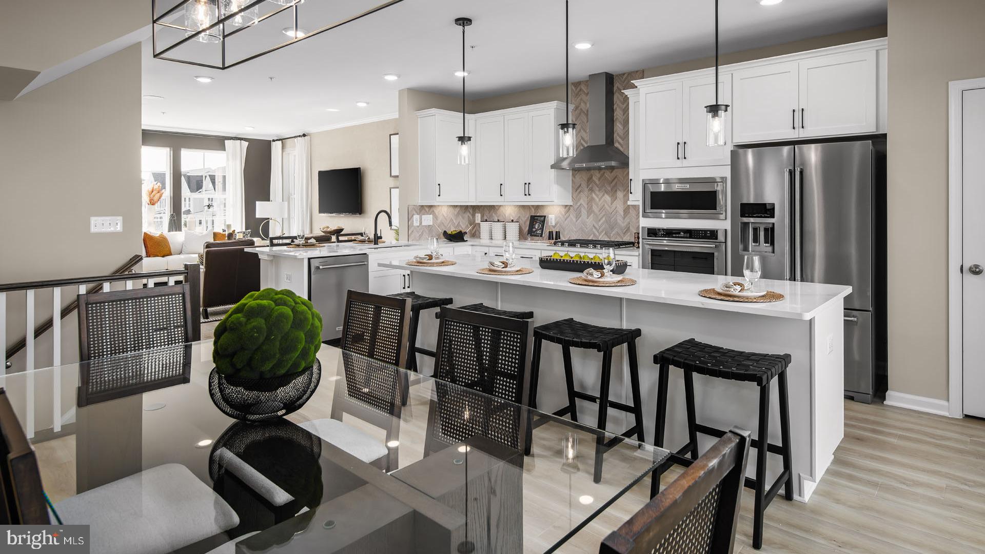 a kitchen with stainless steel appliances kitchen island granite countertop a dining table chairs and a refrigerator