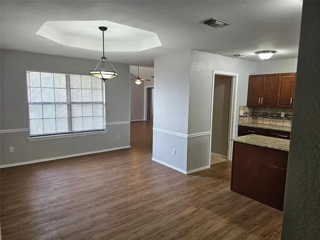 an empty room with wooden floor kitchen view and windows