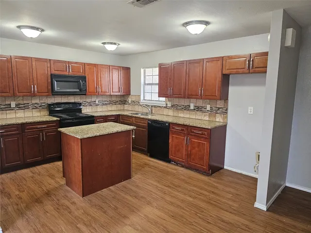 a kitchen with stainless steel appliances granite countertop wooden cabinets a stove top oven a sink and dishwasher with wooden floor