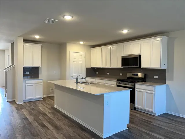 a kitchen with stainless steel appliances a sink dishwasher a stove top oven a refrigerator with grey cabinets and wooden floor